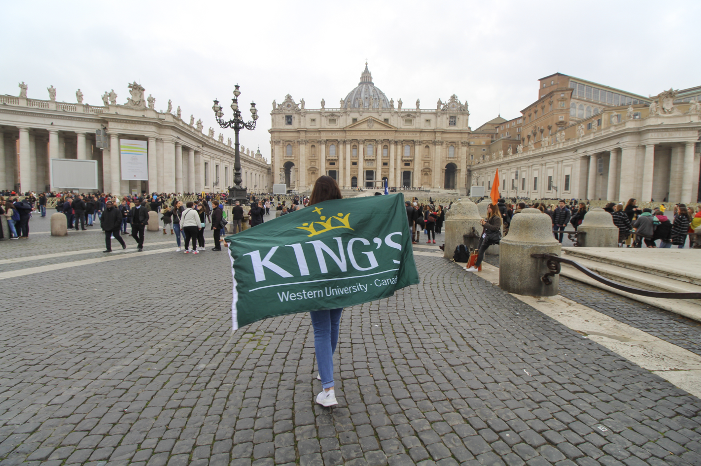 A student carrying a King’s flag across a European city square